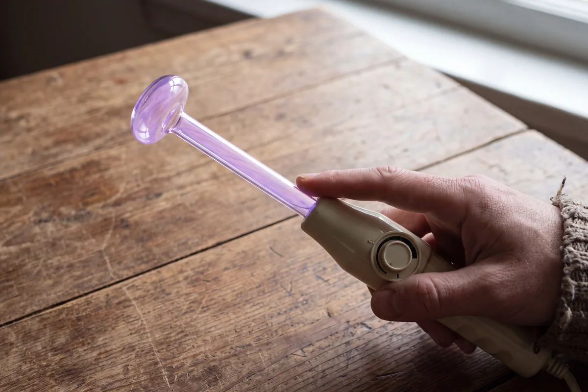 Hand holding a high frequency wand over a dry table with an argon mushroom electrode glowing violet